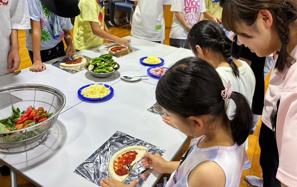 【7月農学校　夏野菜ピザ作り】畑で収穫した野菜を使ったオリジナルのピザづくり。学生がサポートしながら、子どもたちがピザをつくる様子