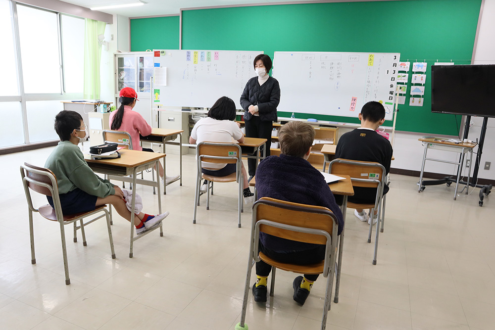 大きな窓から日の光が差し込んだ教室で5名の児童が先生の授業を受けている。