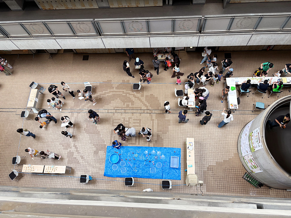 会場となった南講義棟のロビーを上から撮影した写真。数十名の来場者がワークショップを楽しむ様子が見える。